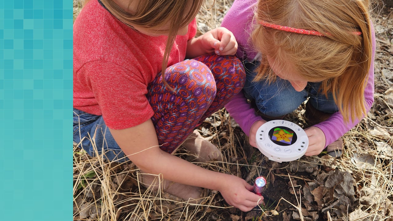 Two first grade students using the Xploris All-in-One-STEAM solution to measure temperature of soil outside.