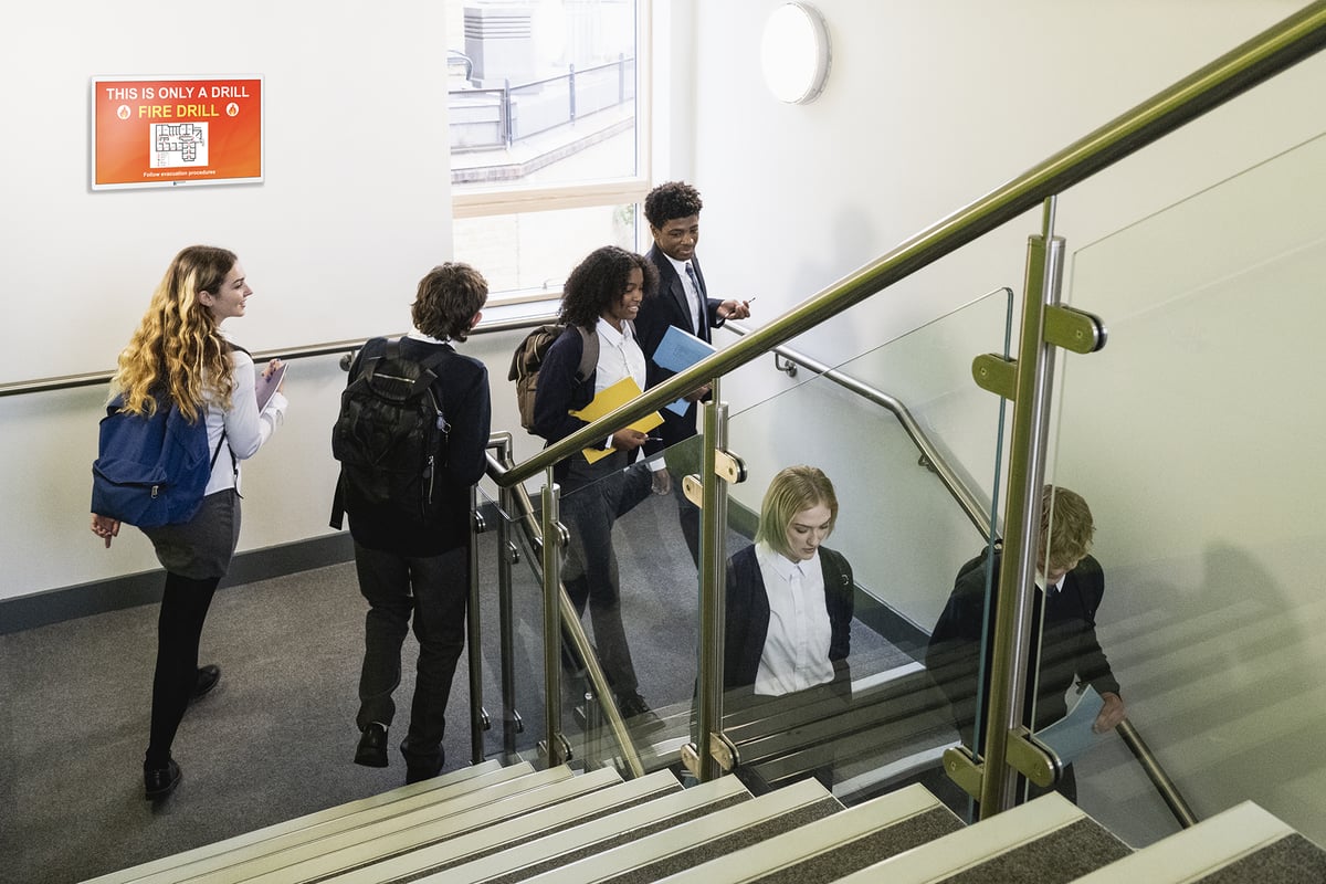 High school students walking through a hallway. TimeSign screen shows Fire Drill alert. 